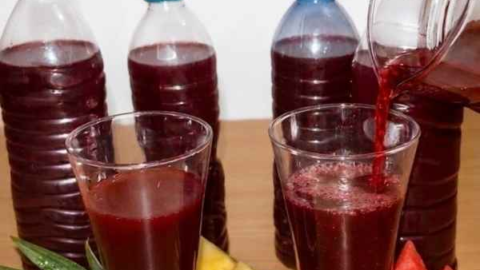 Fruity zobo drink being poured from a jug into a glass container, surrounded by pineapple, watermelon, ginger slices, cloves, and dates