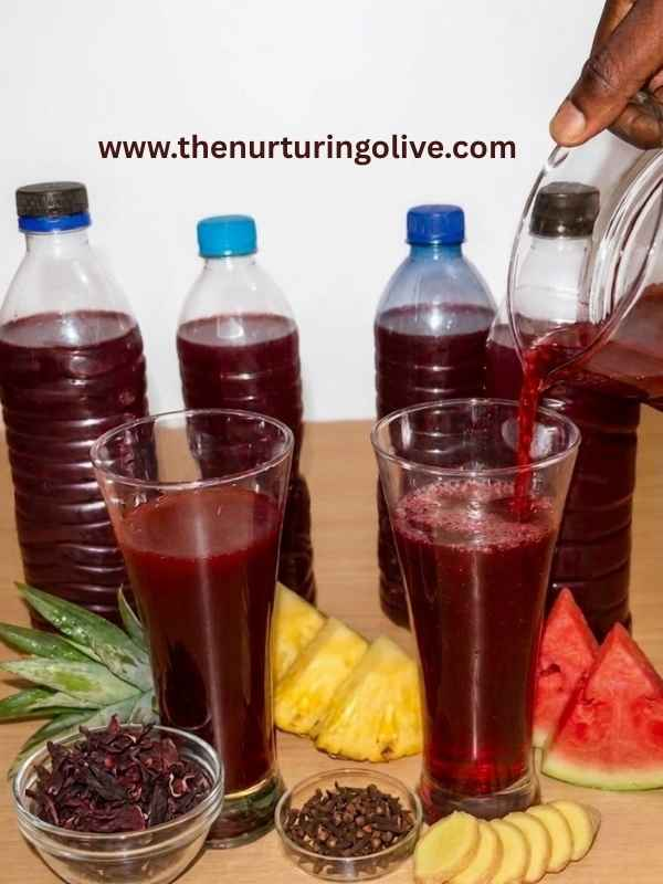 Fruity zobo drink being poured from a jug into a glass container, surrounded by pineapple, watermelon, ginger slices, cloves, and dates